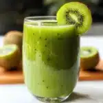 A glass of green kiwi smoothie garnished with a fresh kiwi slice